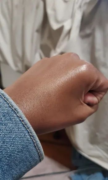 A reviewer showing off the glowy moisturizer as it shines on their hand.