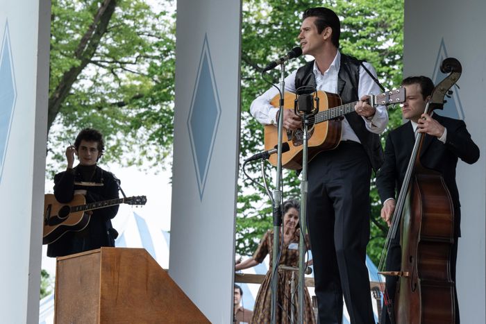 A group of musicians performing on an outdoor stage; the lead vocalist strums a guitar while others play guitar and upright bass.