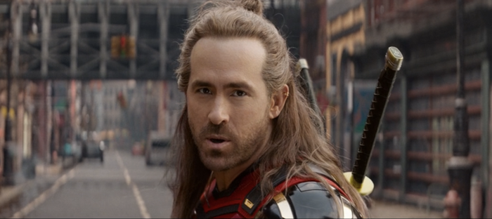 A character with long hair and swords on their back stands on a city street, gazing intently forward, possibly from an action-packed TV or movie scene.