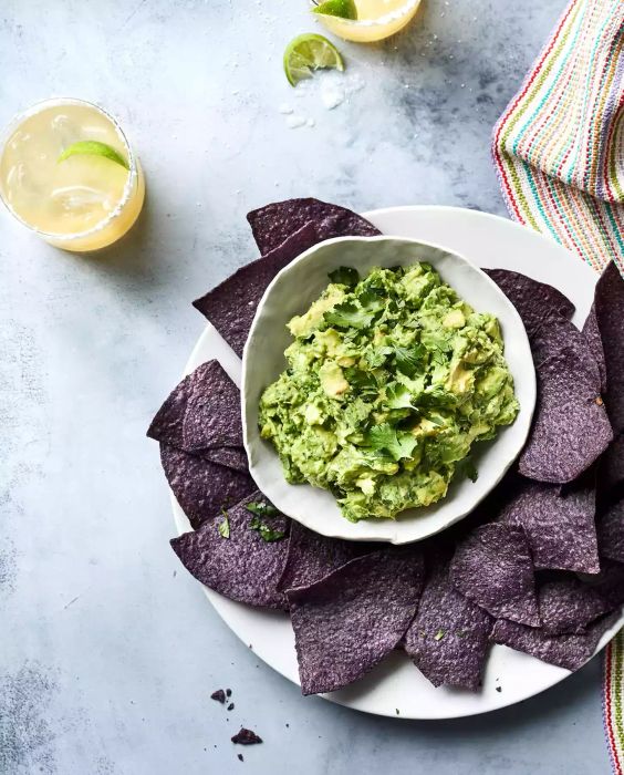 Homemade Guacamole in a white bowl served alongside blue corn tortilla chips