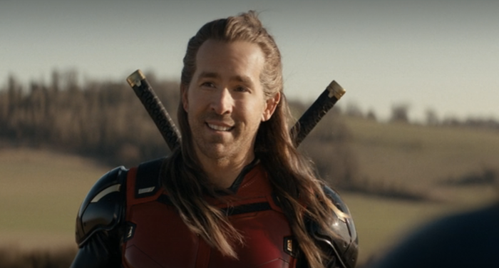 An actor in a superhero costume with long hair stands outdoors, with two swords visible on their back. The scene is likely from a TV show or movie.