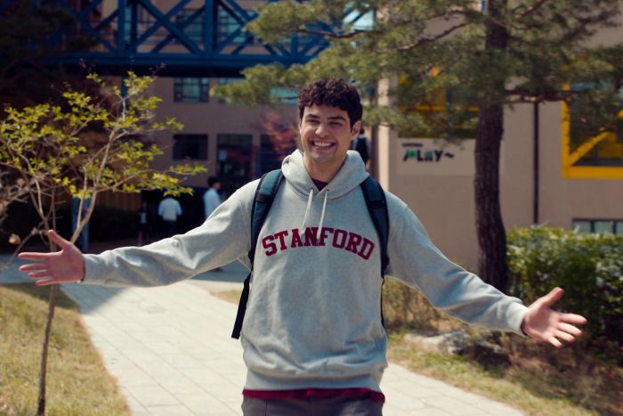 Peter Kavinsky flashing a wide grin, arms stretched out in excitement, wearing a Stanford sweatshirt.