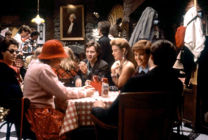 A group of people enjoying a meal and conversation in a bustling restaurant or bar, seated at a table with a checkered cloth