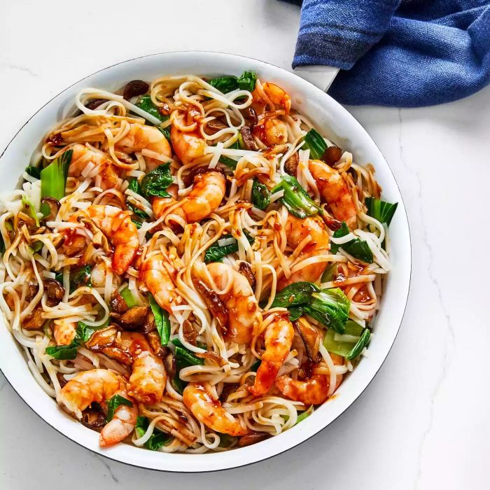 A vibrant stir-fry featuring saucy shrimp and noodles, elegantly presented in a white bowl atop a marble countertop.