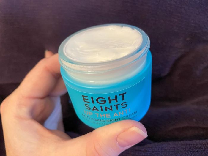 A hand holding a jar of Eight Saints Up The Anti Anti Aging Night Cream with the lid open, showing the cream inside