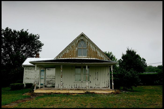 An aged, worn house with a sloping roof, surrounded by tall grass, evoking a sense of nostalgia