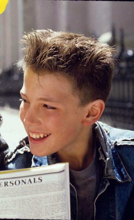 Two young individuals sit outdoors, reading a newspaper titled