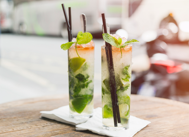 Two mojito glasses sitting on a sidewalk cafe table
