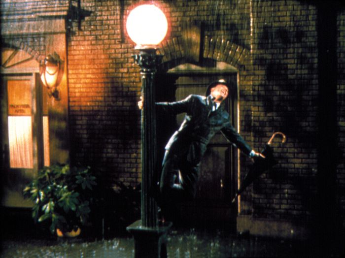 A person happily swinging on a lamppost in the rain, holding an umbrella, recalling a classic movie moment