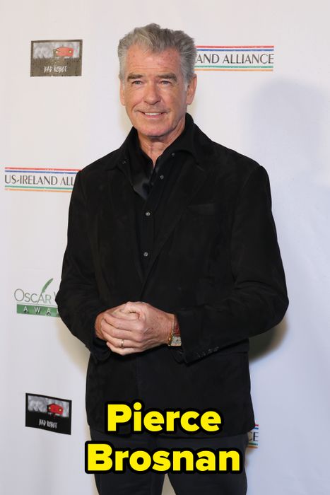 A person dressed in formal wear stands against an event backdrop, smiling and posing gracefully