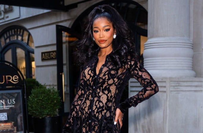 A person wearing a sheer lace dress with a matching underslip, striking a confident pose on a city sidewalk
