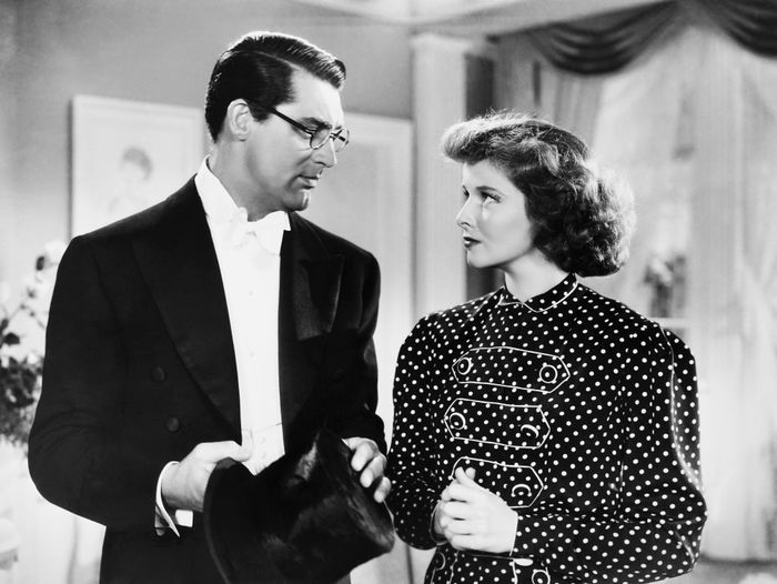Two individuals in elegant outfits from a classic film scene: one wearing a tuxedo and holding a top hat, the other dressed in a polka dot gown, gazing at one another