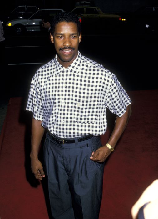 A person dressed in a checkered shirt and trousers on the red carpet, smiling at the camera