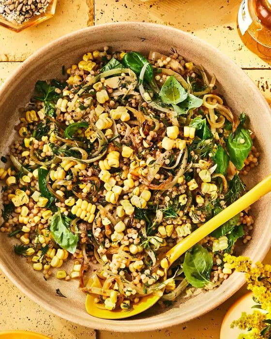 Toasted Israeli Couscous with Corn and Herbs Served in a Large Bowl with a Yellow Serving Spoon
