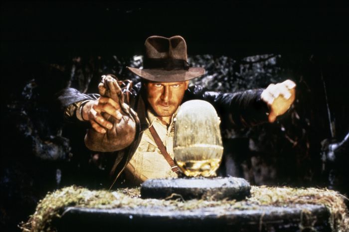 An archaeologist in adventure gear carefully reaches for a golden idol in a tense moment of suspense