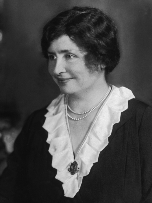 A woman in early 20th-century fashion, featuring a layered neckline and a pearl necklace, captured in a vintage portrait