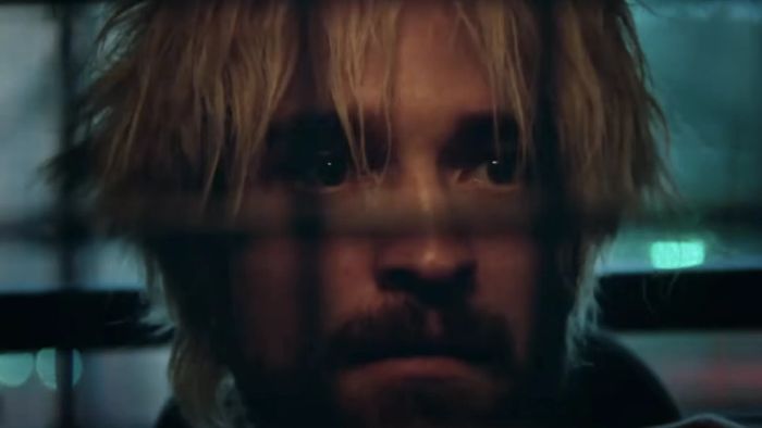 Robert, with disheveled hair and a tense expression, peers through prison bars, capturing a moment of intense drama.