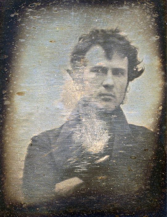 A classic photograph of a man with a serious demeanor, dressed in a dark coat, staring directly at the camera.