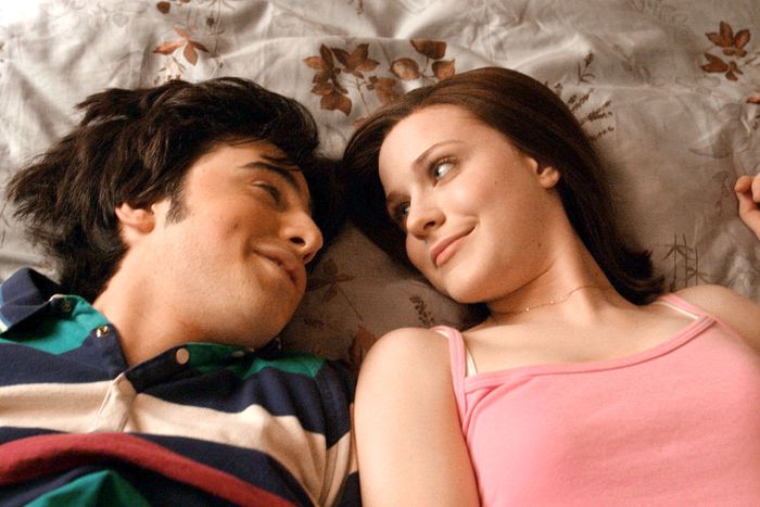 Two people lying next to each other on a bed, smiling gently as they gaze into one another's eyes