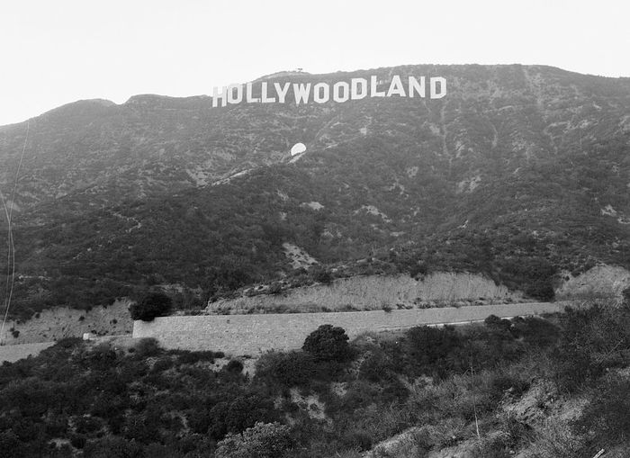 A black-and-white photo of the original 'Hollywoodland' sign nestled on the hillside in Los Angeles, CA.