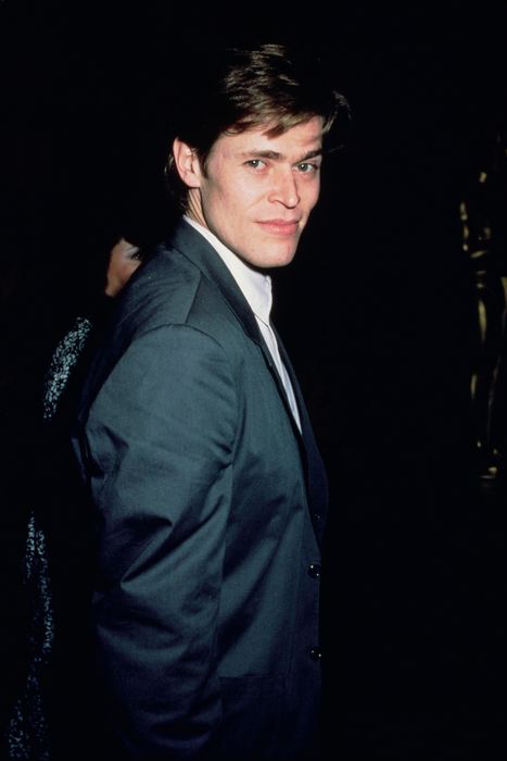 A person in a formal suit, with a slight smile, slightly angled to the side, in a refined setting