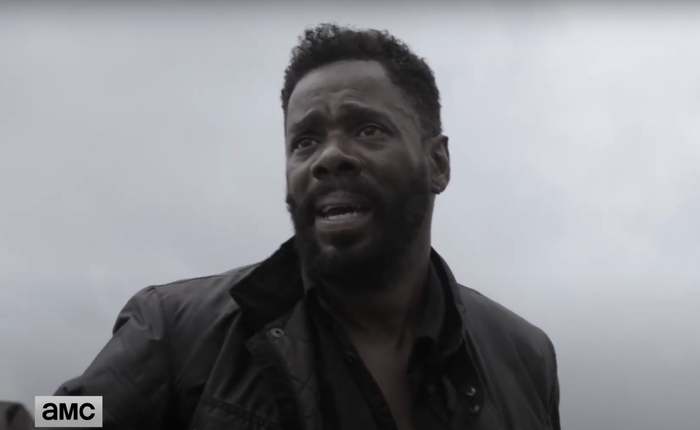 Colman, sporting a beard and dark jacket, gazes into the distance with a concerned expression. The 
