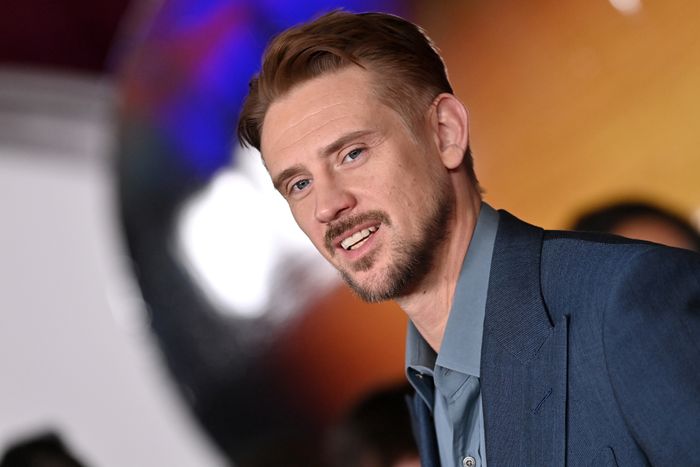 A man dressed in a blue suit with a casual shirt, smiling and gazing away from the camera. The scene suggests a formal or media-related event.