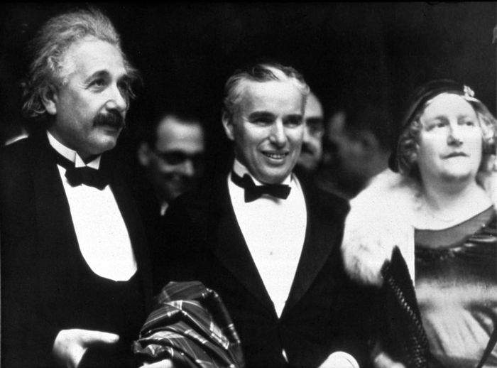 Albert Einstein and Charlie Chaplin in tuxedos, accompanied by Elsa, Einstein's wife, in an elegant dress at a formal event.
