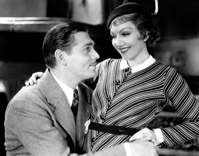 A couple from a classic film era sitting closely, the woman in a striped dress and beret, smiling affectionately at the man in a suit
