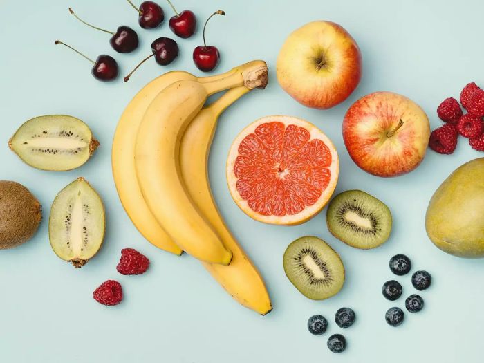 A vibrant flat lay featuring fresh banana, grapefruit, berries, and apples. Captured indoors with strobe lighting from above.