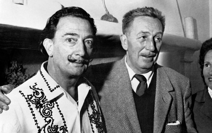 Two men with distinct mustaches, dressed in 1950s formal clothing, pose together with smiles in a classic black-and-white photograph.