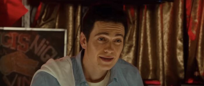 Hayden, dressed casually with a towel draped over his shoulder, smiles faintly in front of a curtain backdrop.