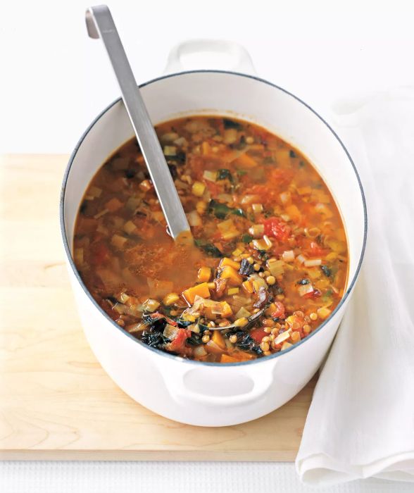 Brown Lentil Soup with Kale and Sweet Potatoes Served in a Large White Pot with a Metal Ladle