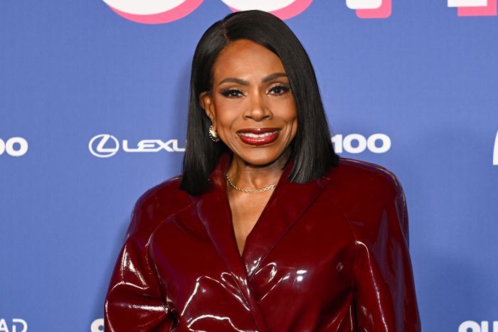 Sheryl Lee Ralph grins on the red carpet, dressed in a shiny, sophisticated coat with a sleek and stylish look.