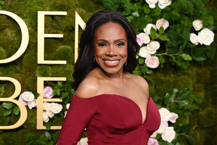 Sheryl Lee Ralph beams with a smile, donning an off-shoulder dress in front of a floral backdrop at a public event.