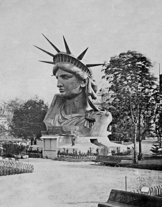 A historic image of the Statue of Liberty's head and shoulders, displayed at the 1878 Paris World Fair before being assembled in New York Harbor.