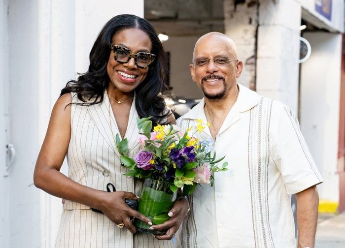 Sheryl Lee Ralph, holding a small bouquet of flowers, stands with her husband Vincent Hughes, both dressed in casual yet fashionable attire.