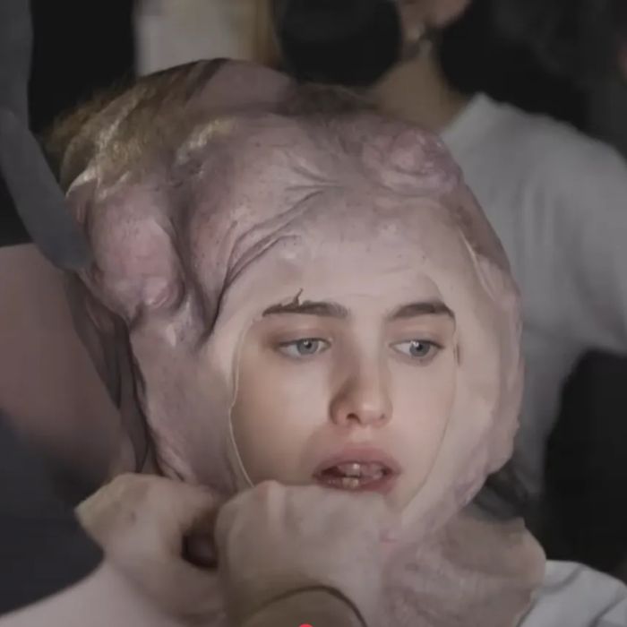 Margaret sits as a makeup artist applies special effects makeup to her head and neck, transforming her appearance into an alien-like form.