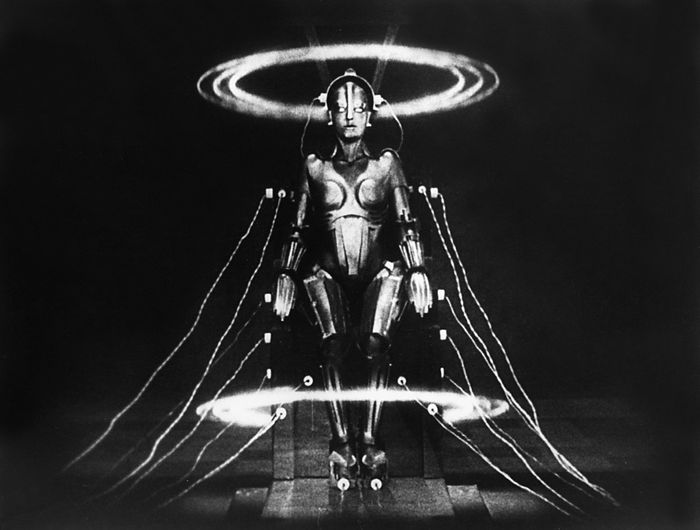 A humanoid robot seated in a chair, encircled by radiant rings and intricate wiring, from the iconic sci-fi classic 'Metropolis.'