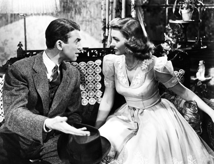 A vintage movie moment features a man in a suit and a woman in a classic dress sitting on a sofa, deeply engrossed in conversation