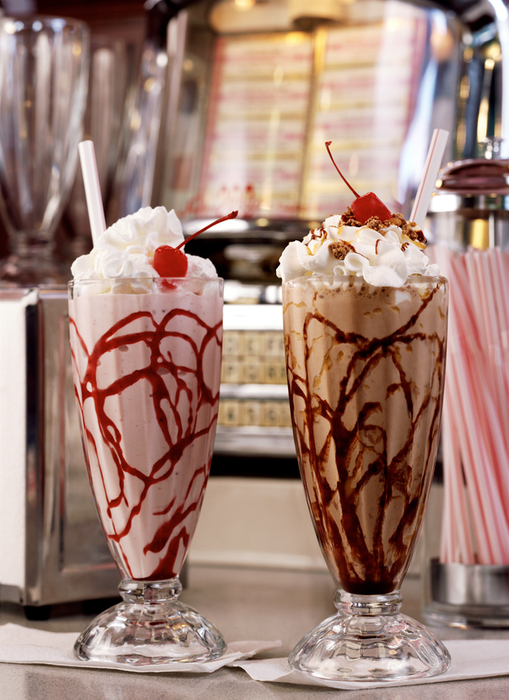 Two sundaes placed on a diner counter, surrounded by straws, napkins, and an old-fashioned juke box in the background.