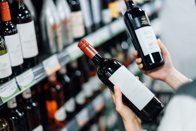 Overhead view of a woman picking red wine bottles from a supermarket shelf in the liquor section
