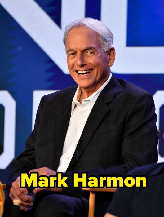 A man in a black suit and white shirt sits and smiles during a panel discussion event