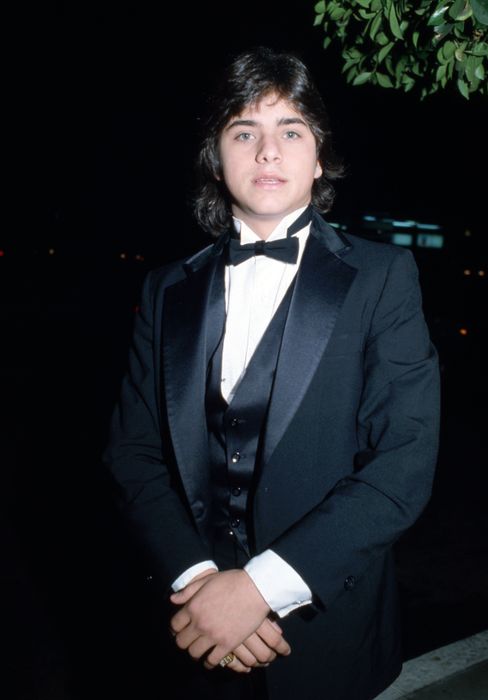 A young individual dressed in a tuxedo with a bow tie, standing outdoors at a formal gathering