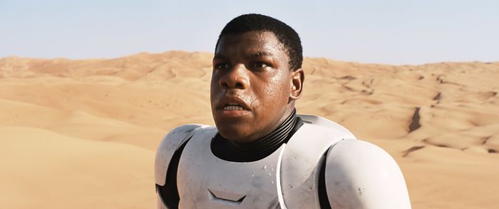 John, clad in futuristic armor, stands in a vast desert, looking pensive.