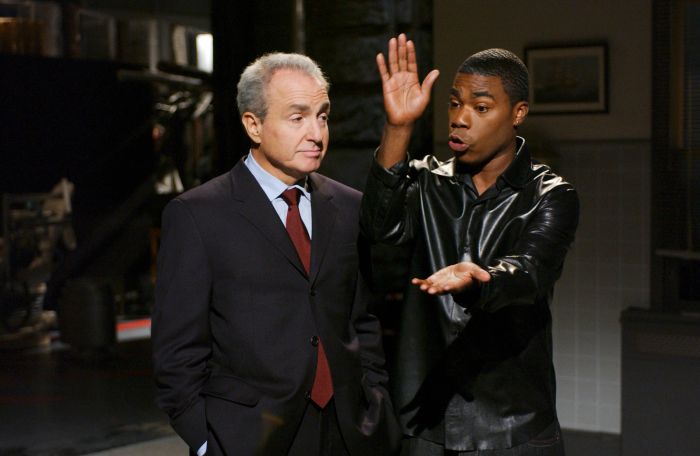 Lorne and Tracy are seen having a conversation on set, one gesturing passionately while the other listens attentively, dressed in a suit.