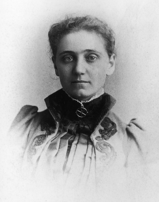 A vintage portrait of a woman dressed in Victorian-era attire, featuring intricate embroidery on her high-collared gown