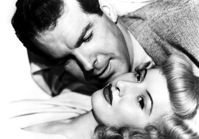 A black-and-white close-up shot of a man and a woman with 1940s hairstyles, lying next to each other, staring off into the distance