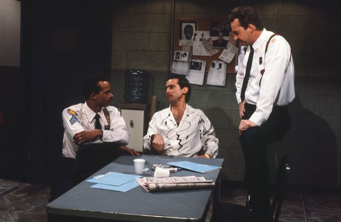 Three men in police uniforms engage in a conversation around a table in a police station setting.