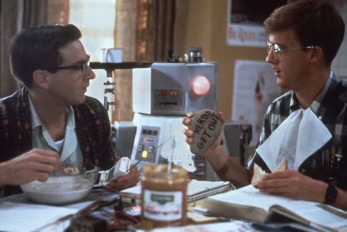 Two individuals sitting at a table surrounded by books, a robot, and a sign that reads 